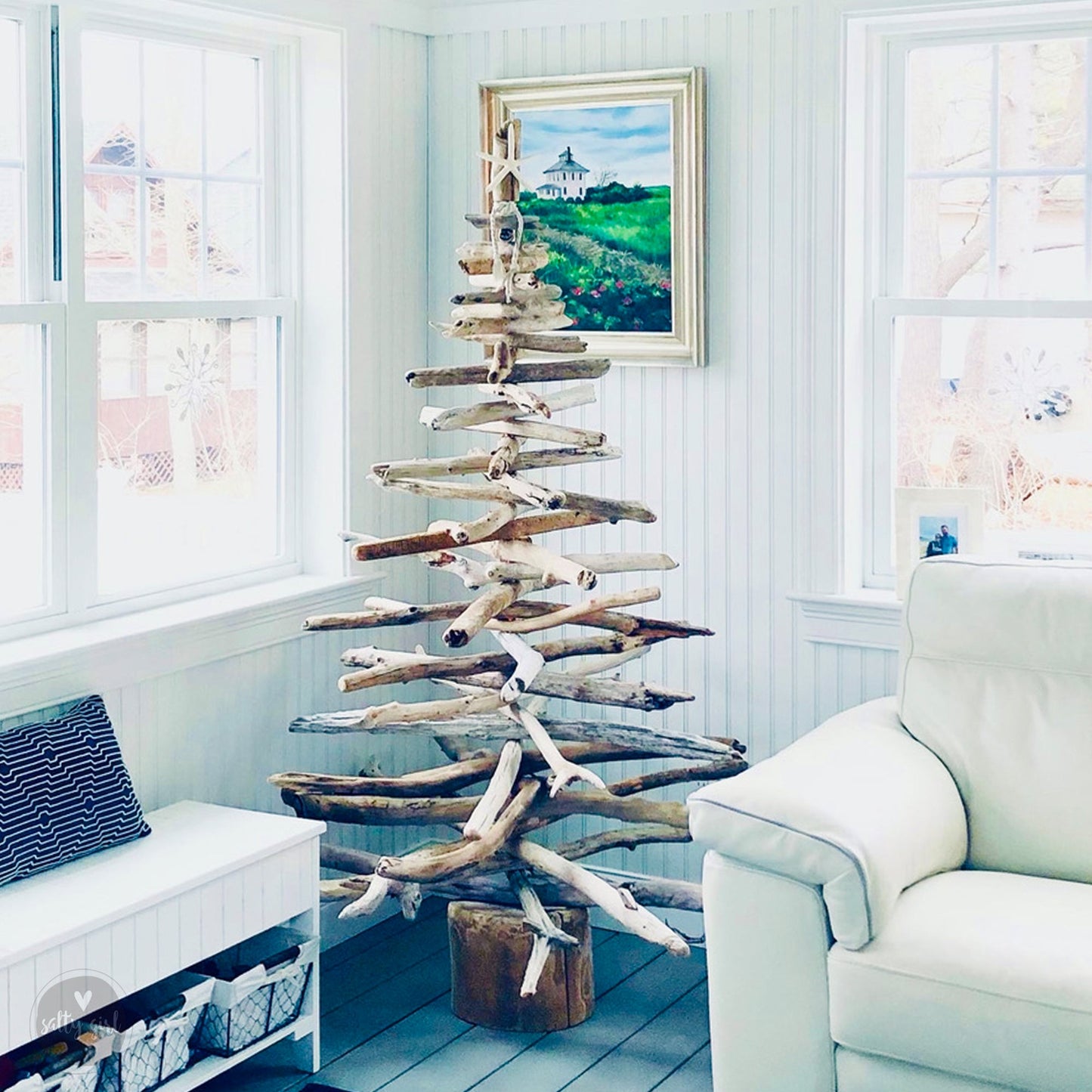 Christmas tree made of driftwood, displayed in a living room setting with a white chair and a painting on the wall.