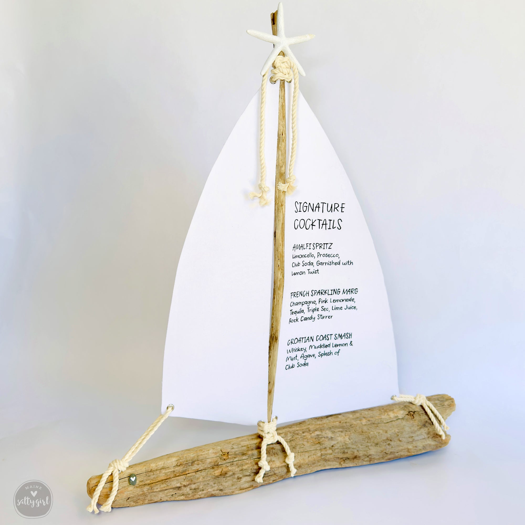 A white sailboat-shaped cocktail menu with a wooden base, displaying a list of signature cocktails.