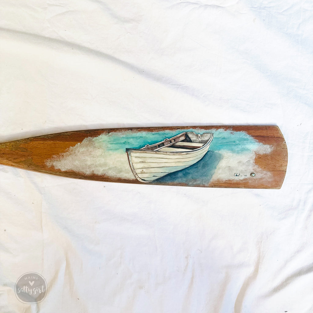 a wooden paddle with a painted image of a boat on it.