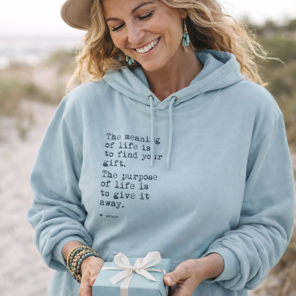 A smiling woman wearing a light blue Maine Salty Girl hoodie with a quote printed on it, holding a gift box with a bow.