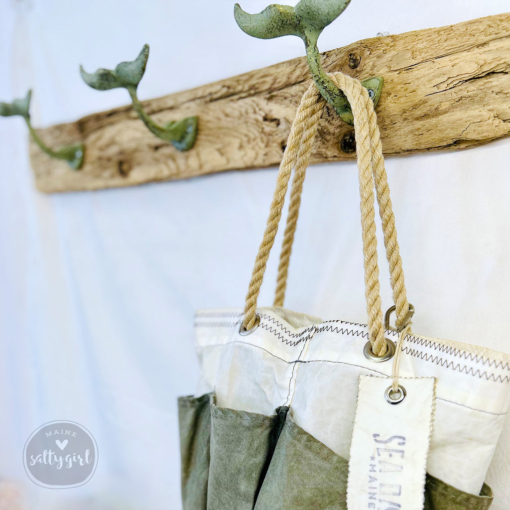 A wooden coat rack with two green metal hooks and a white and green bag hanging from the hooks.