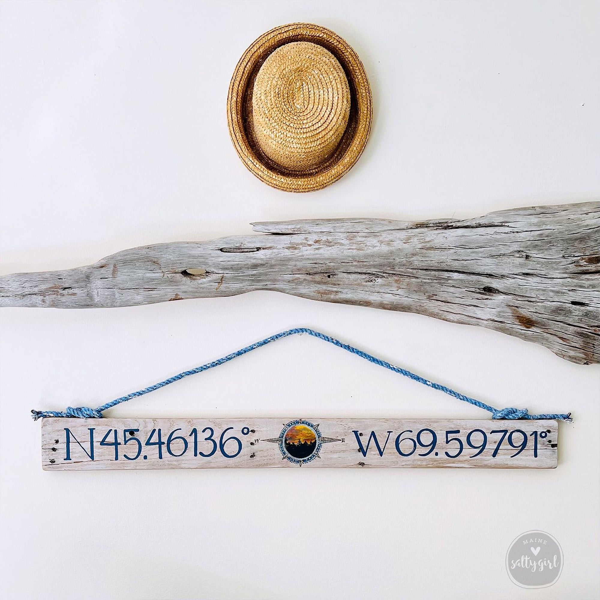 a wooden sign with a compass rose and a straw hat, all hanging on a white wall.