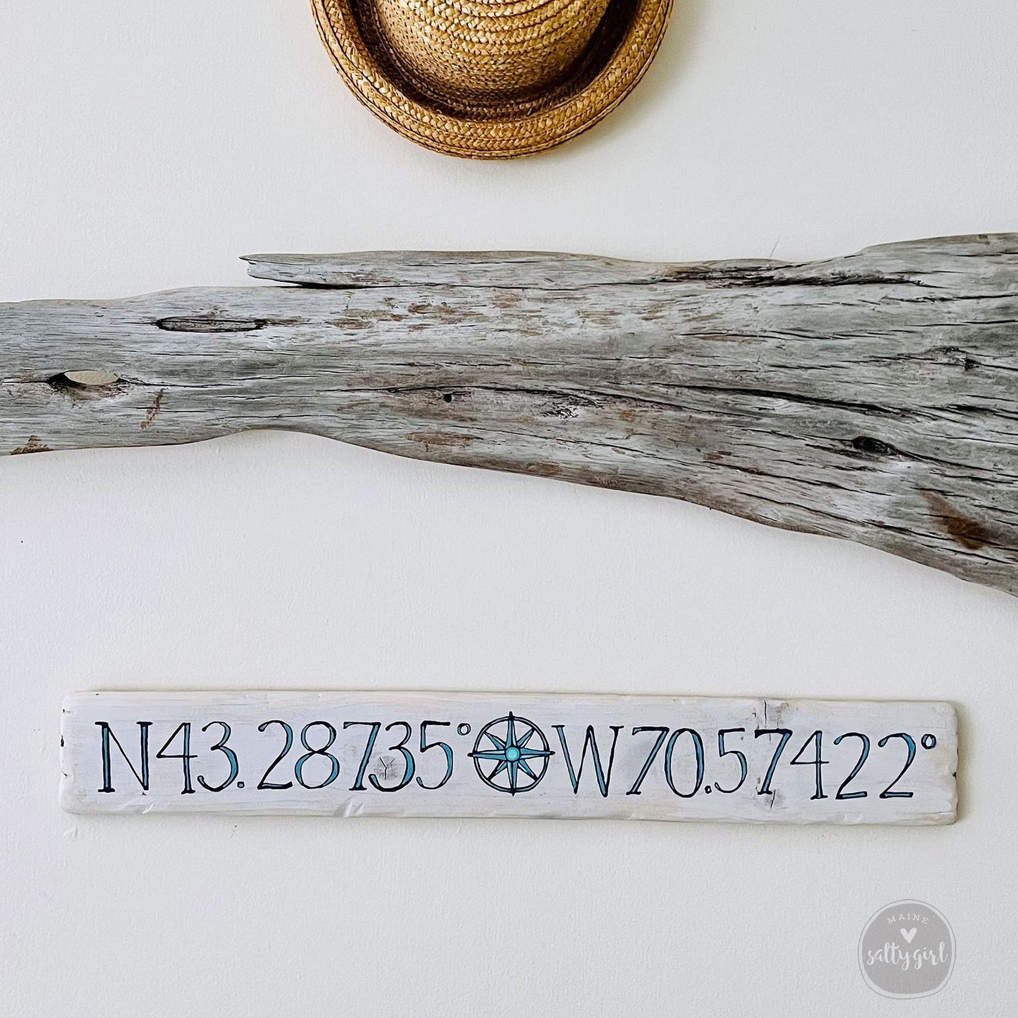 a wooden sign with a compass rose and a straw hat on a white wall.