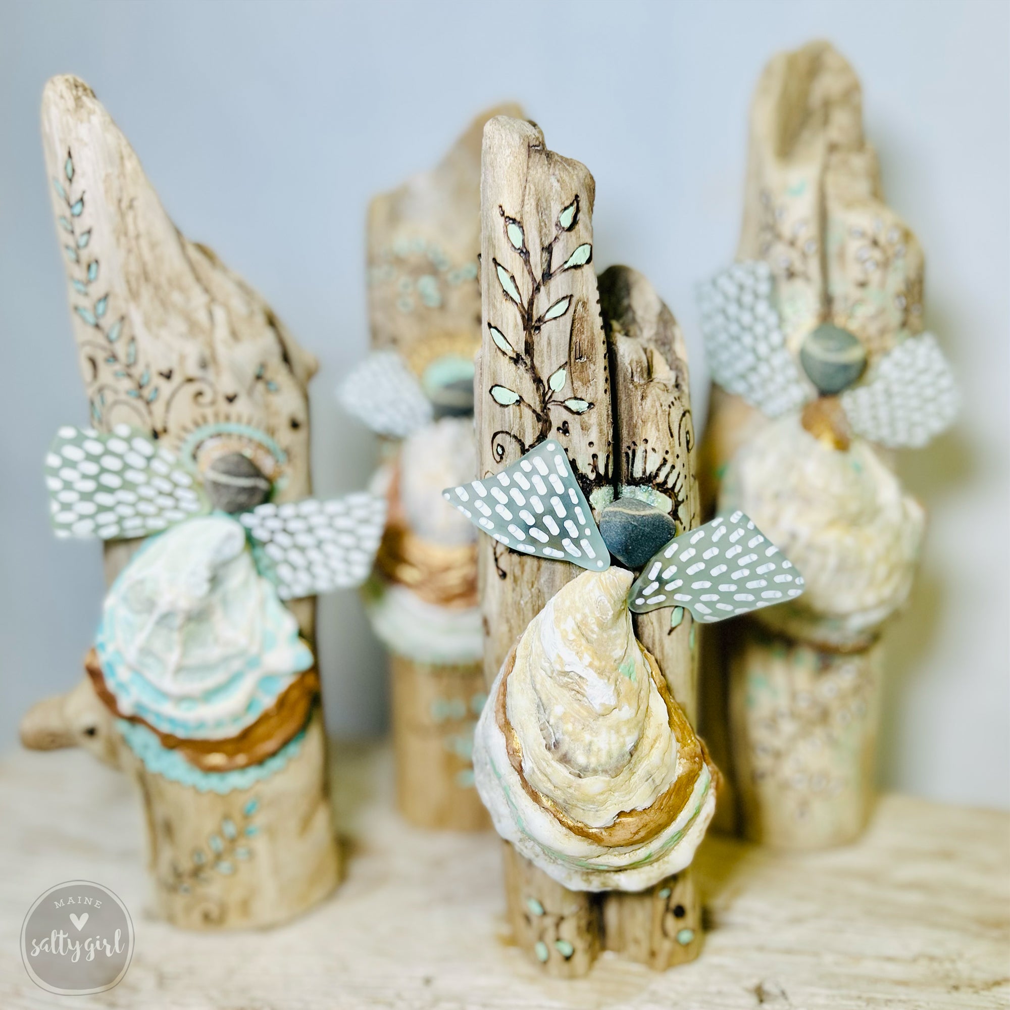 a collection of intricately carved wooden angel figurines, each with unique designs and patterns. The angels are crafted from driftwood and are displayed on a wooden surface, creating an artistic and visually appealing arrangement.