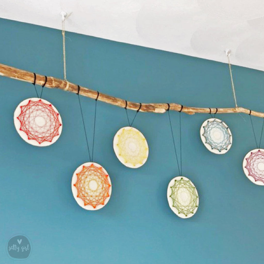 a collection of colorful dreamcatchers hanging from a wooden branch against a blue wall.