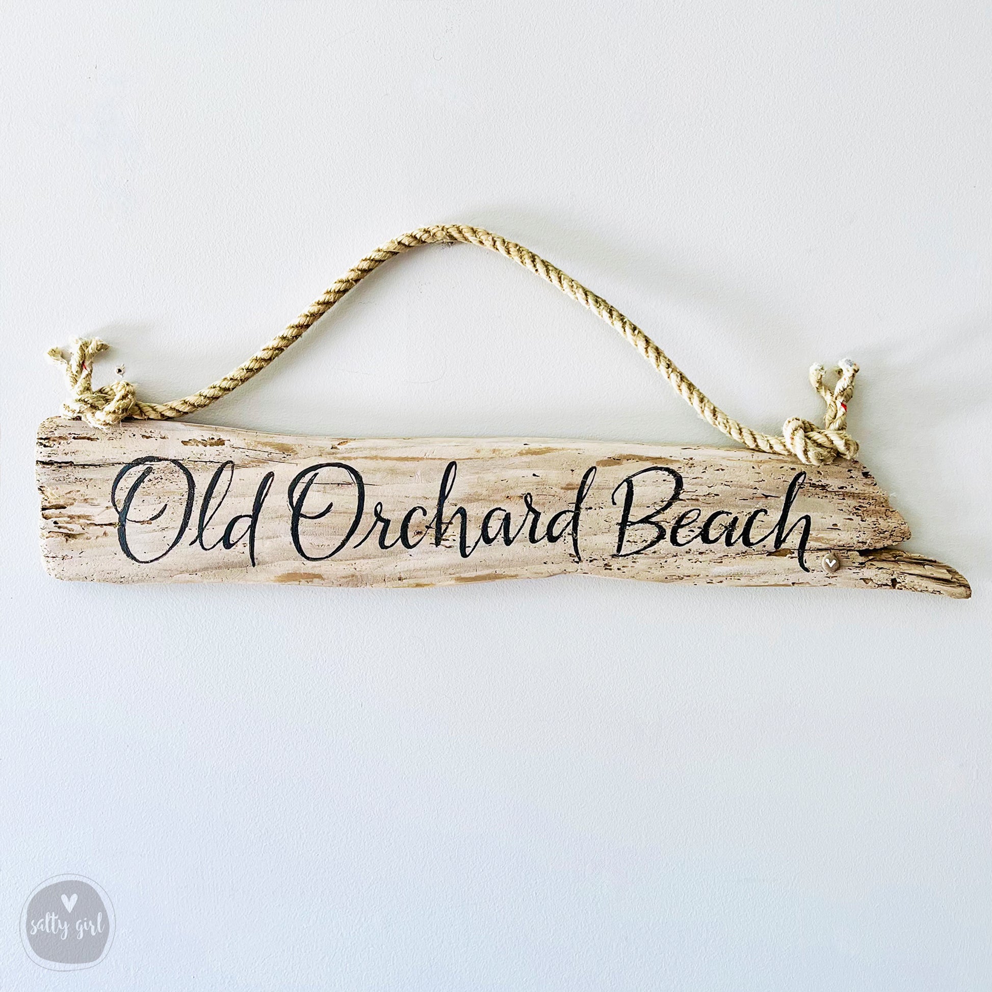 A wooden sign with the text "Old Orchard Beach" written on it, hanging from a rope.