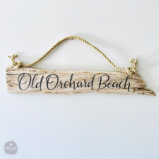 A wooden sign with the text "Old Orchard Beach" written on it, hanging from a rope.