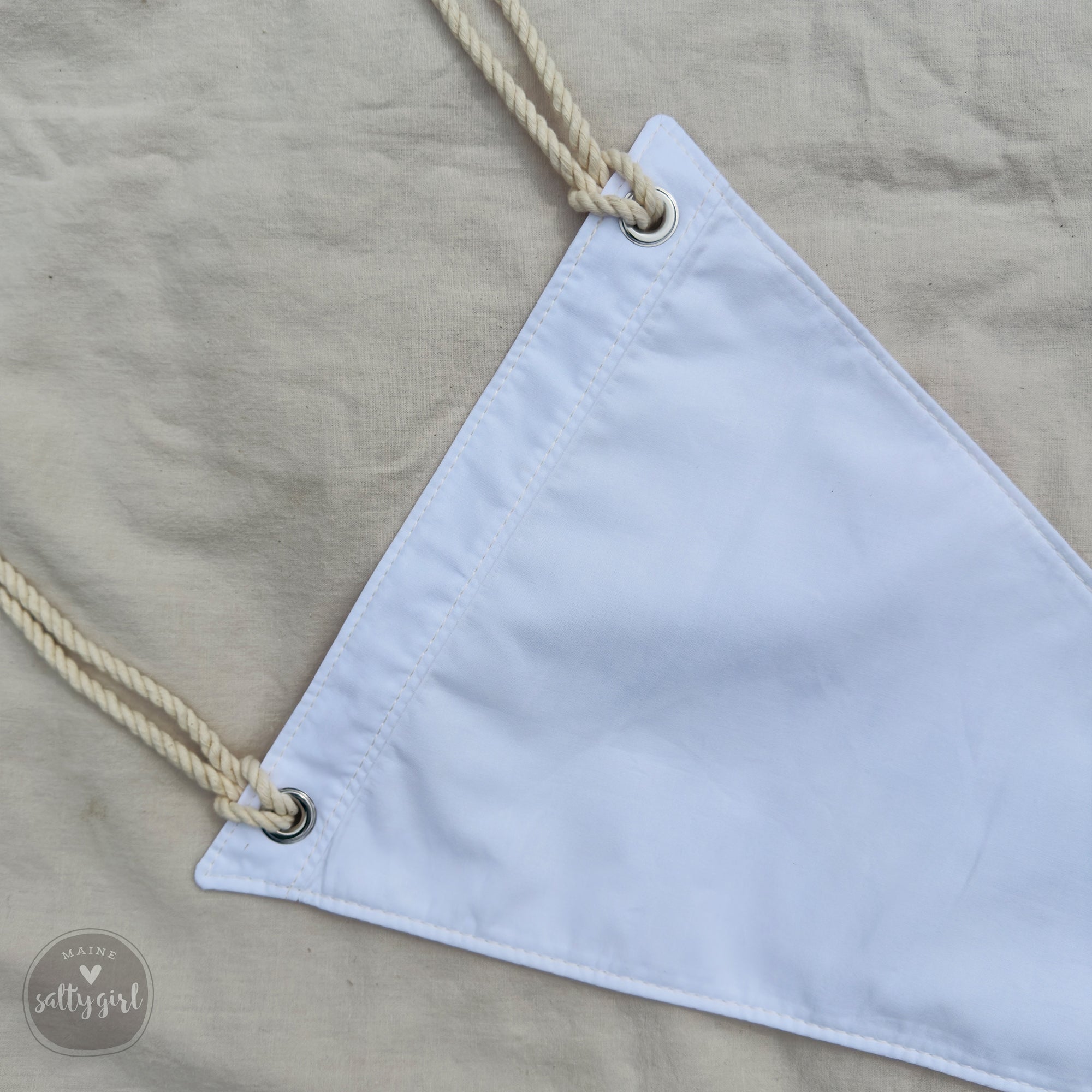 A white triangular flag or banner with two ropes attached to it, resting on a beige fabric background.