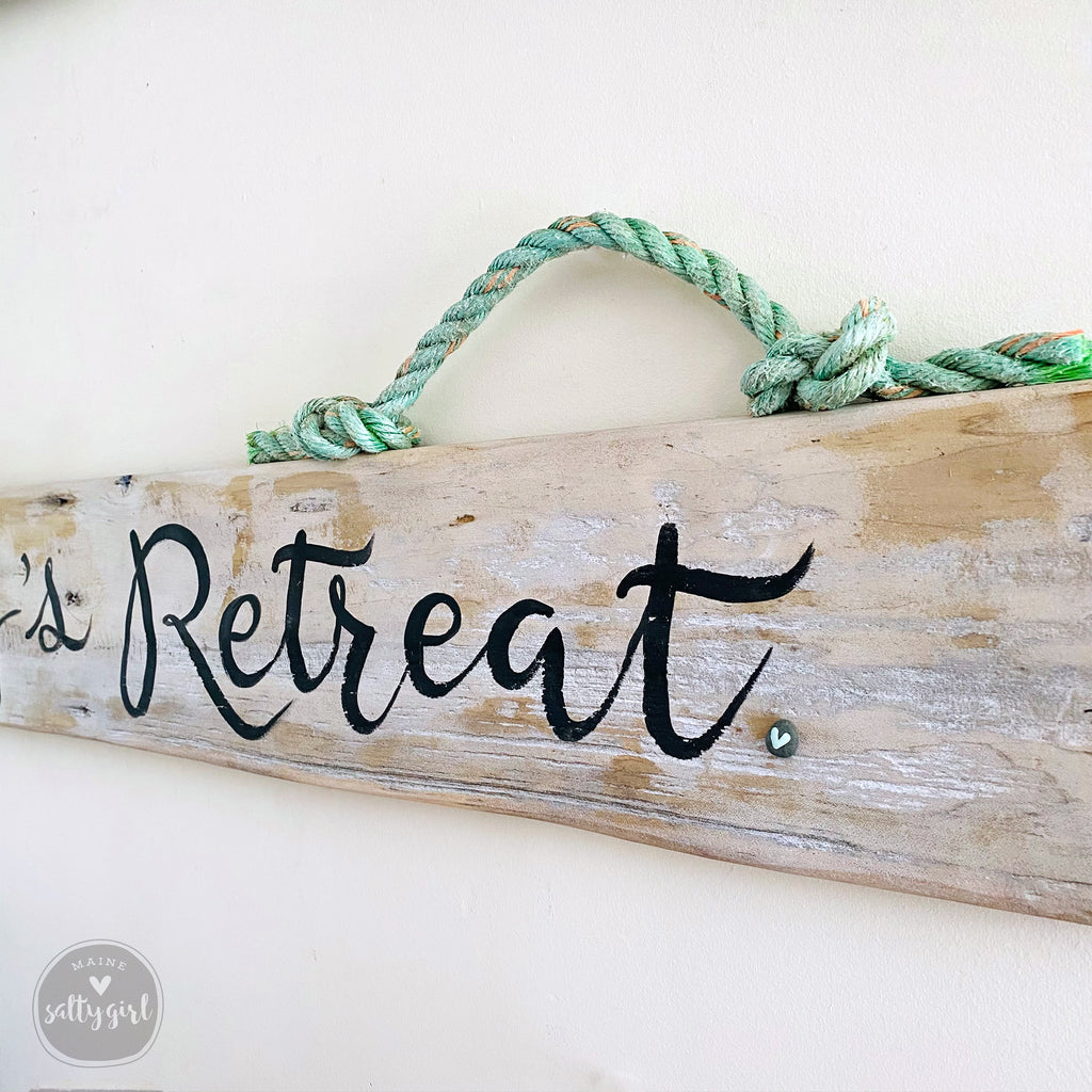 A wooden sign with the word "Retreat" written on it, attached to a rope.