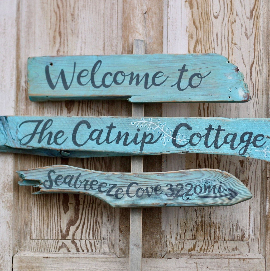 a wooden sign with the text "Welcome to The Catnip Cottage" and "Seabreeze Cove 322m" written on it.