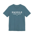 A teal-colored Maine Salty Girl tee with the text "PADDLING LIKE A GIRL" printed on it.