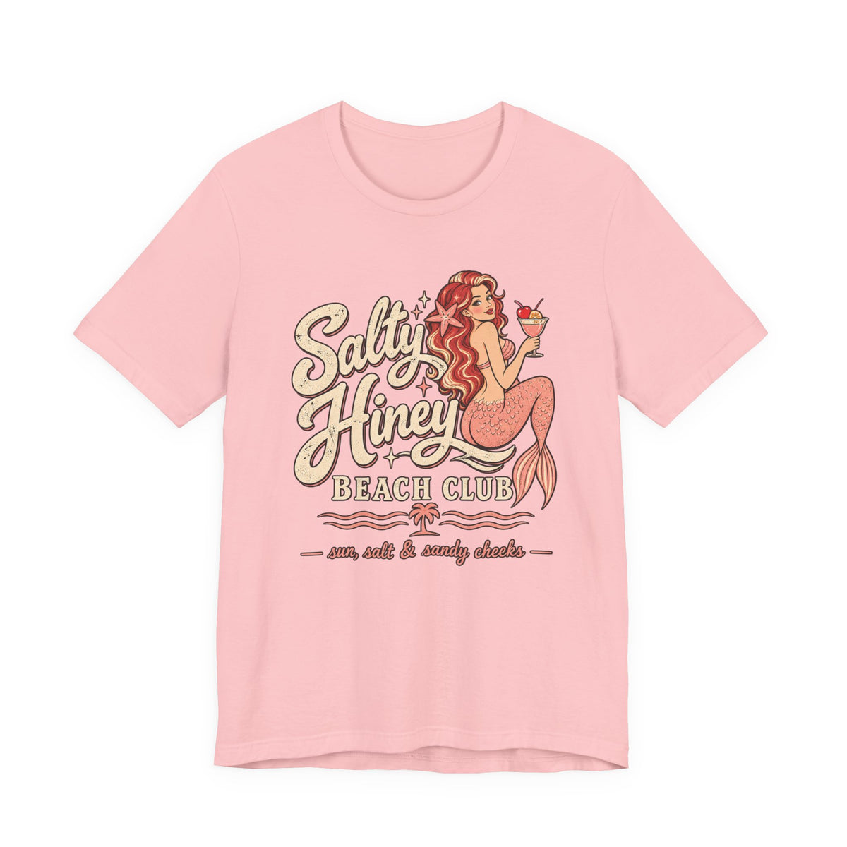 A pink t-shirt with a graphic design featuring a mermaid holding a drink and the text "Salt & Honey Beach Club" along with the phrase "sun, salt & sandy checks".