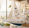 A model sailboat with sail and hull decorations sits on a table, surrounded by various items such as a bowl of fruit, a vase, and other decorative objects.