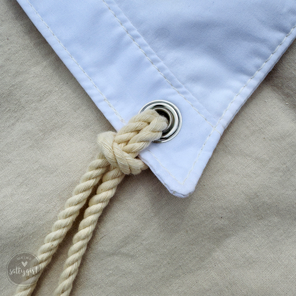 A close-up view of a white fabric with a silver button and a rope tied to it.