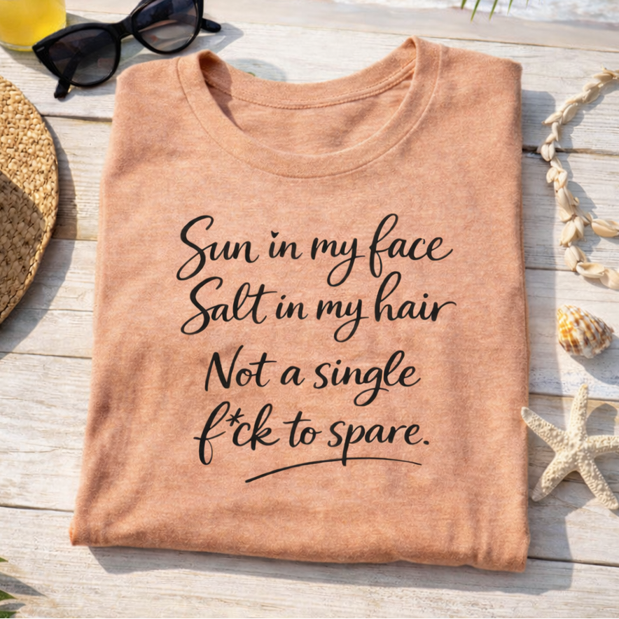 a t-shirt with a humorous text printed on it, placed on a wooden surface with a straw hat, sunglasses, and seashells nearby.