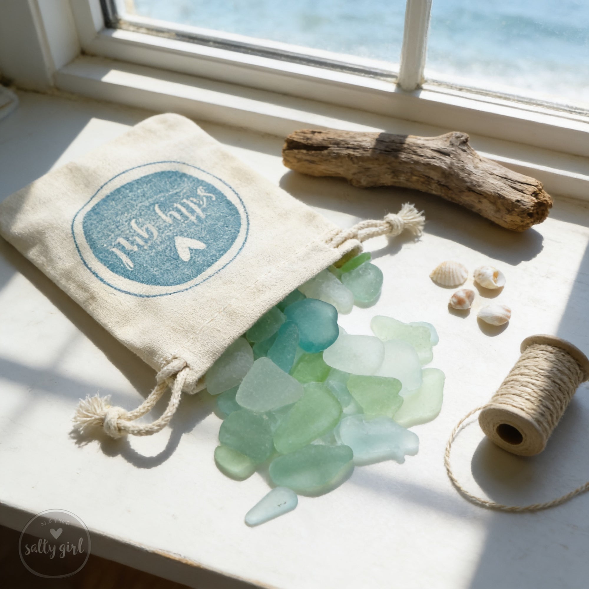A white window sill displays a collection of sea glass, shells, and a spool of twine, creating a nautical-inspired scene.