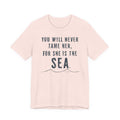 A light pink t-shirt with the text "YOU WILL NEVER TAME HER, FOR SHE IS THE SEA" printed on it.