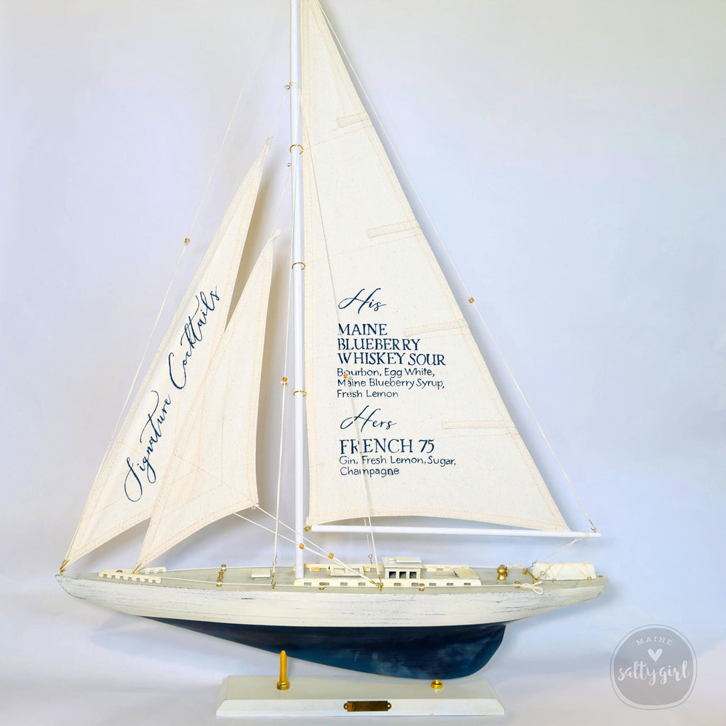 A model of a sailboat with a white sail and blue trim, featuring text that lists the names of the drinks served on the boat.