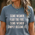 A woman wearing a gray Maine Salty Girl t-shirt with the text "Some women fear the fire. Some women simply become it." printed on it.