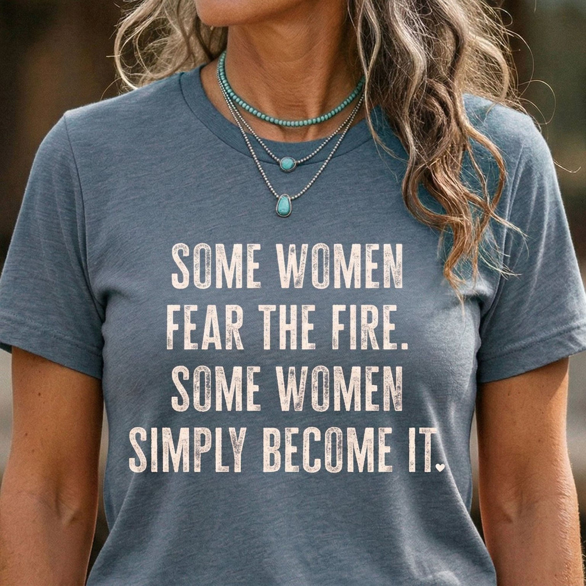 A woman wearing a gray Maine Salty Girl t-shirt with the text "Some women fear the fire. Some women simply become it." printed on it.