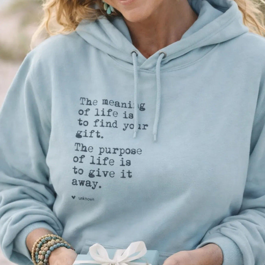 A smiling woman wearing a light blue Maine Salty Girl hoodie with a quote printed on it, holding a gift box with a bow.