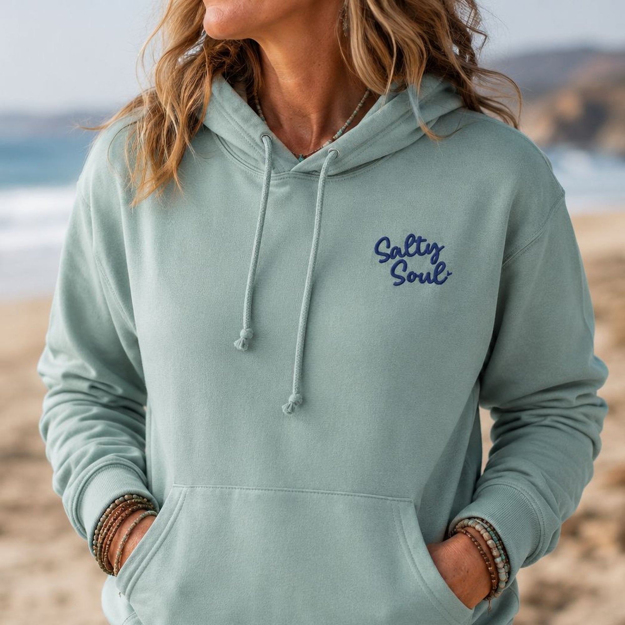 Person wearing a light blue hoodie with 'Salty Soul' text on a beach