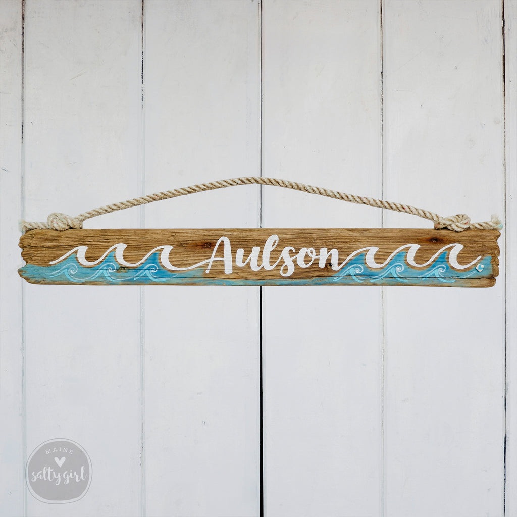 A wooden sign with the name "Aulson" written on it, hanging on a white wooden wall.