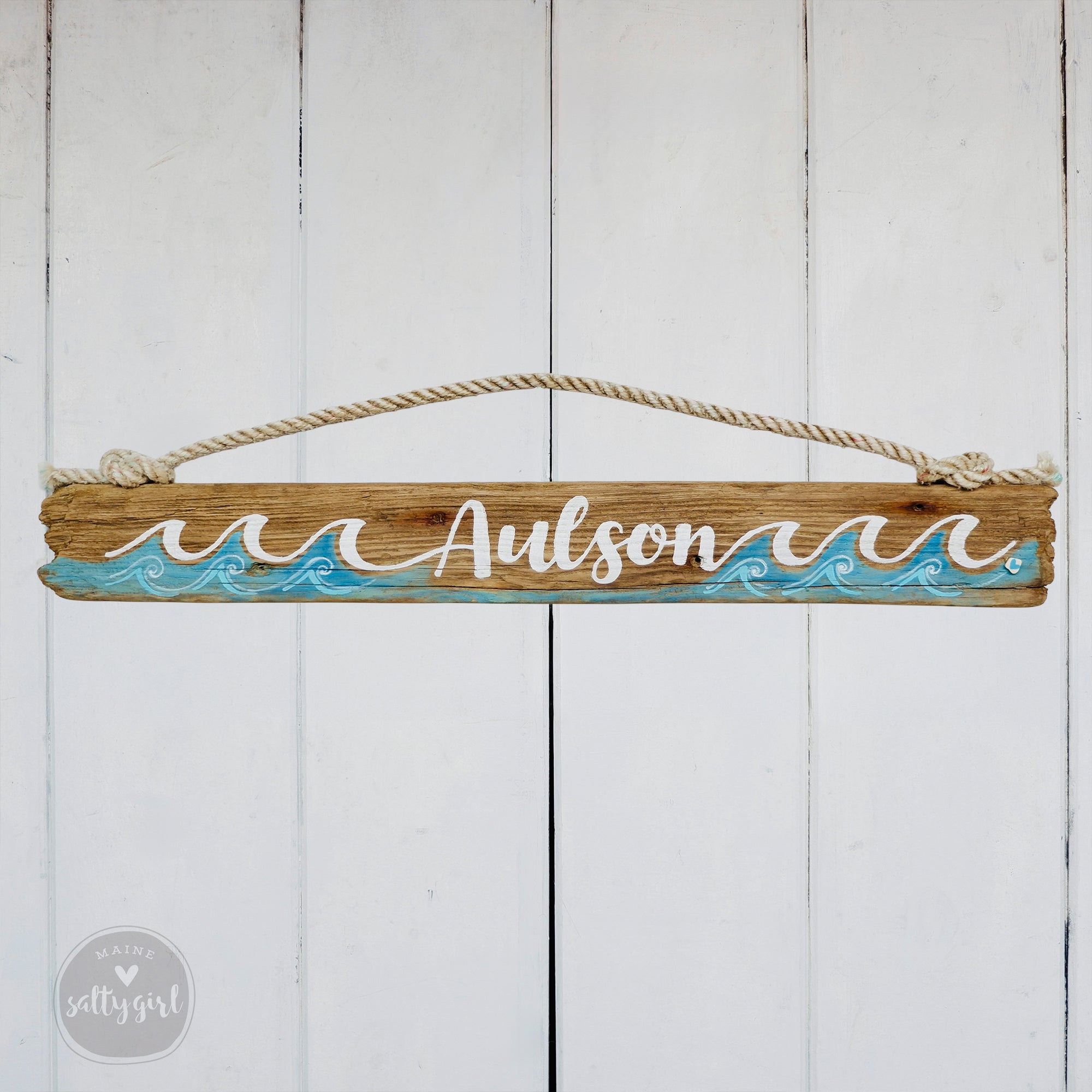 A wooden sign with the name "Aulson" written on it, hanging on a white wooden wall.