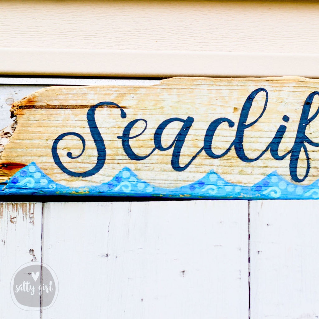 A wooden sign with the word "Seaclf" painted on it, placed on a white wall.