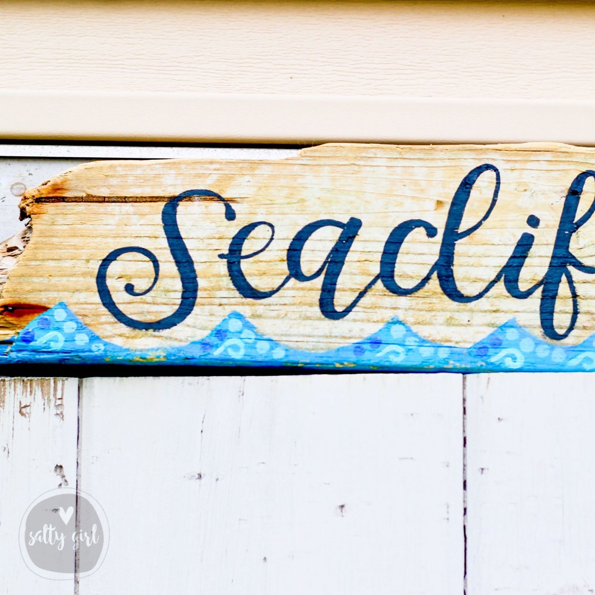 A wooden sign with the word "Seaclf" painted on it, placed on a white wall.