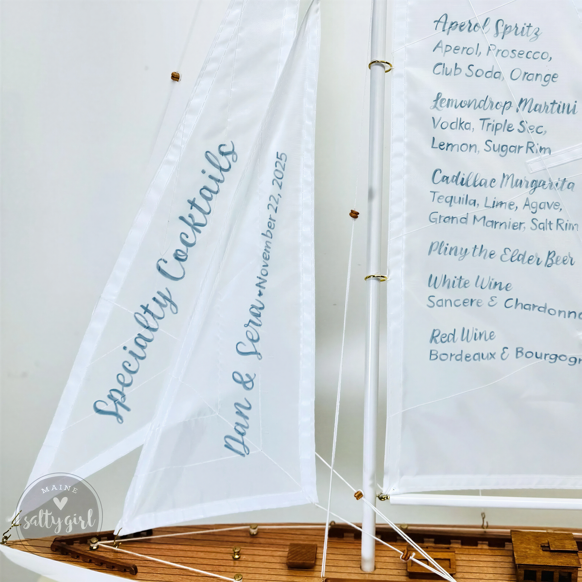A white sailboat with a list of cocktail names on it, including Aperol Spritz, Club Soda, Orange, Lemon Drop, Triple Sec, Cointreau, Garnacha, and White Wine.