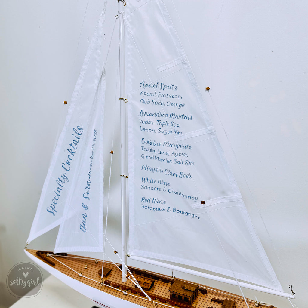 A model sailboat with a menu displayed on its sails, indicating a menu for a special cocktail event.