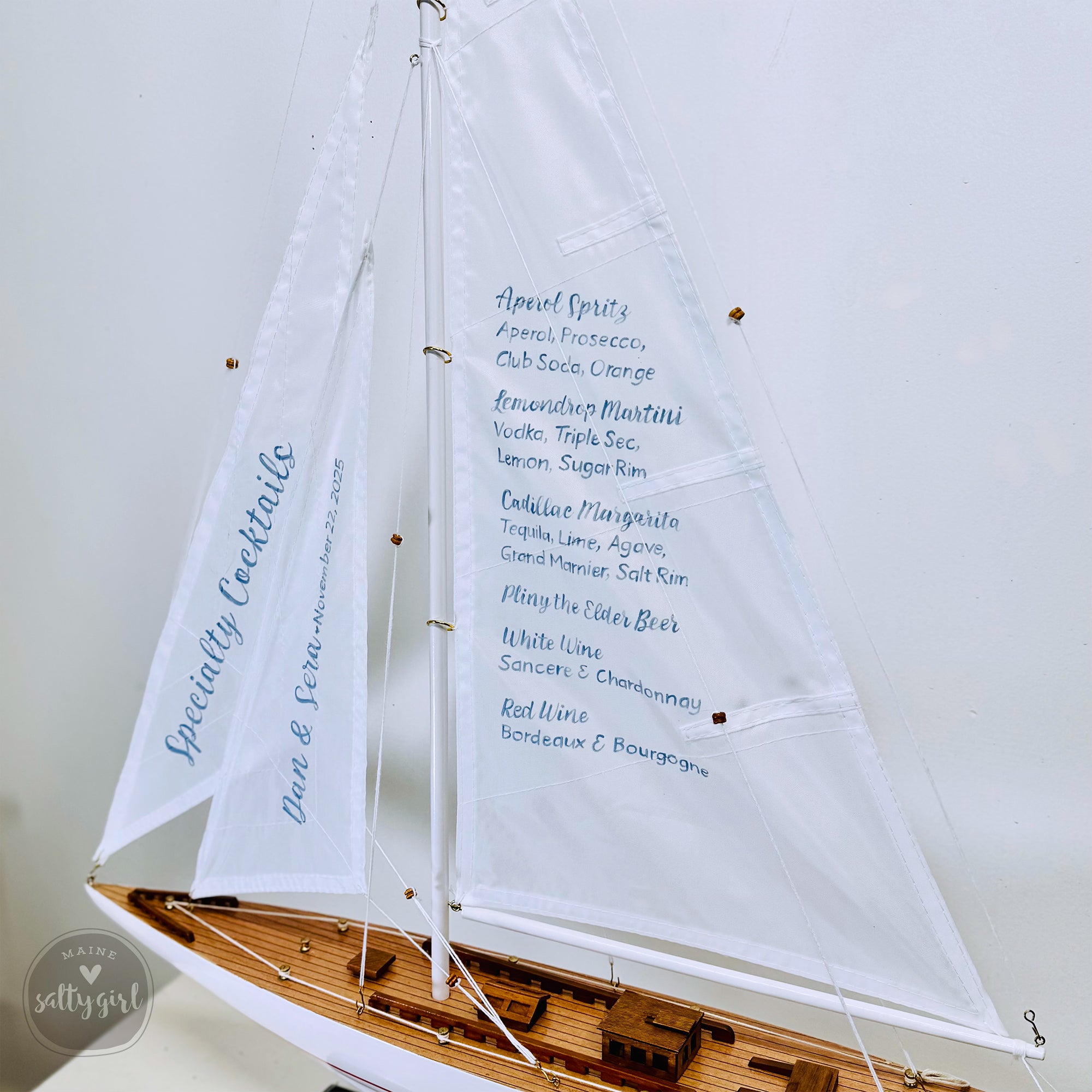 A model sailboat with a menu displayed on its sails, indicating a menu for a special cocktail event.