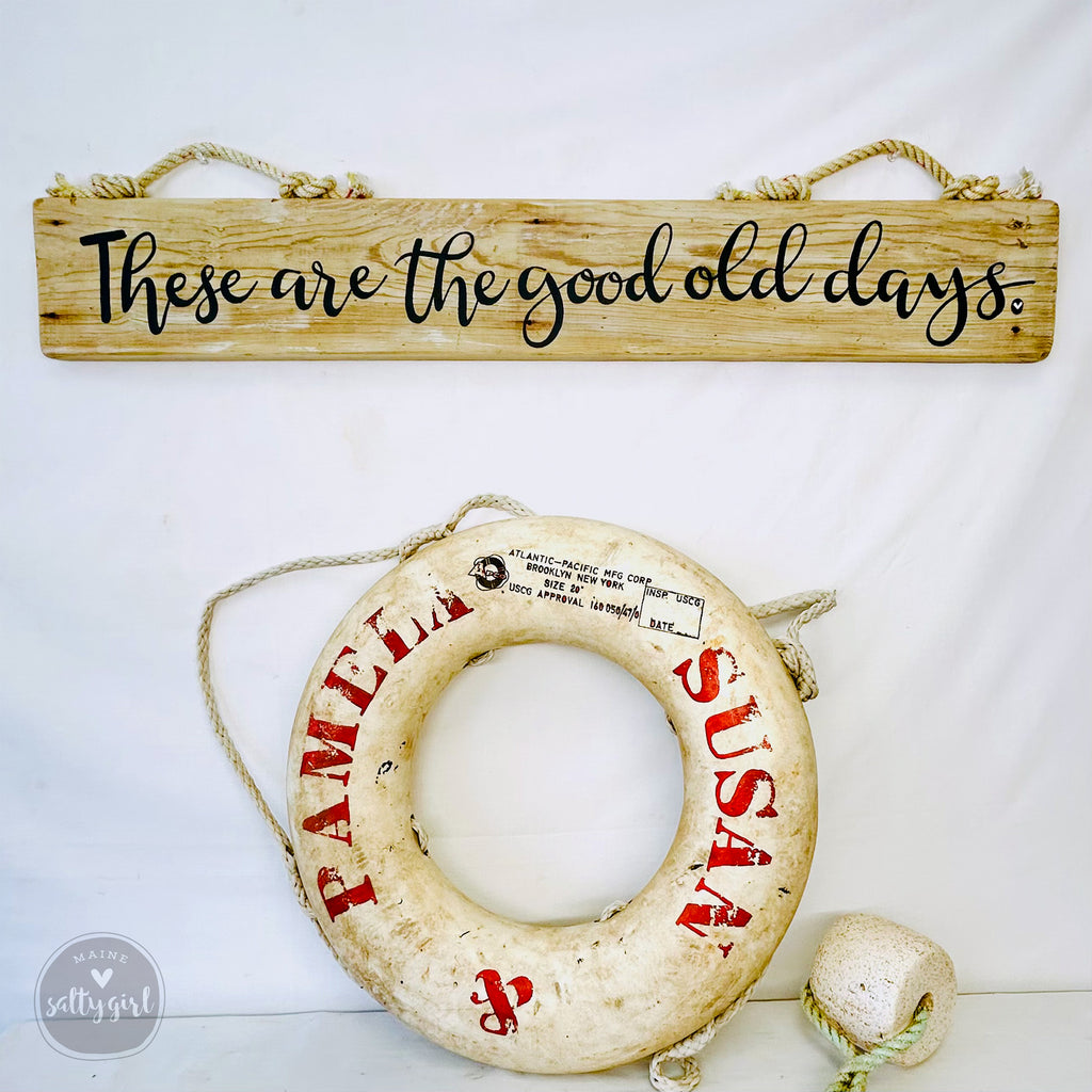 a wooden sign with the text "These are the good old days" and a life preserver with the name "SUSAN" written on it, both hanging on a wall.