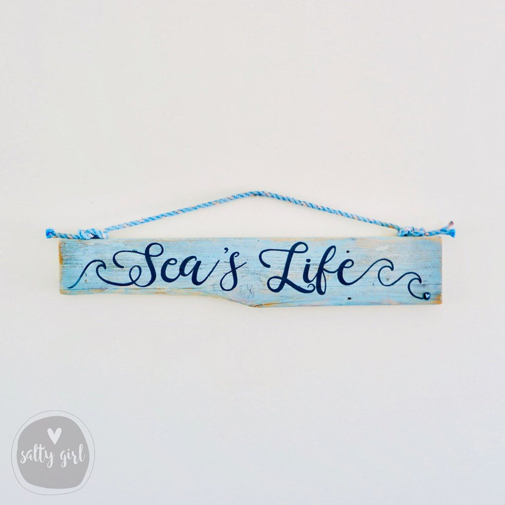 A wooden sign with the text "Sea's Life" written on it, hanging on a wall.