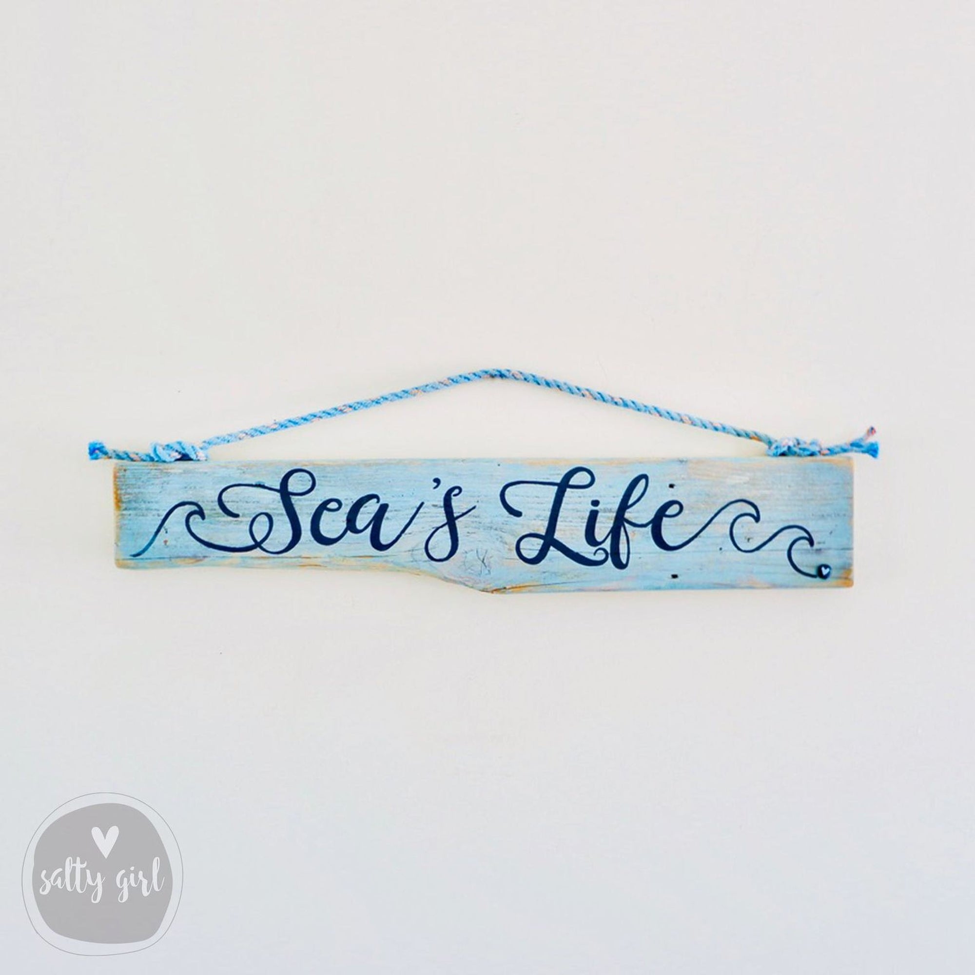 A wooden sign with the text "Sea's Life" written on it, hanging on a wall.