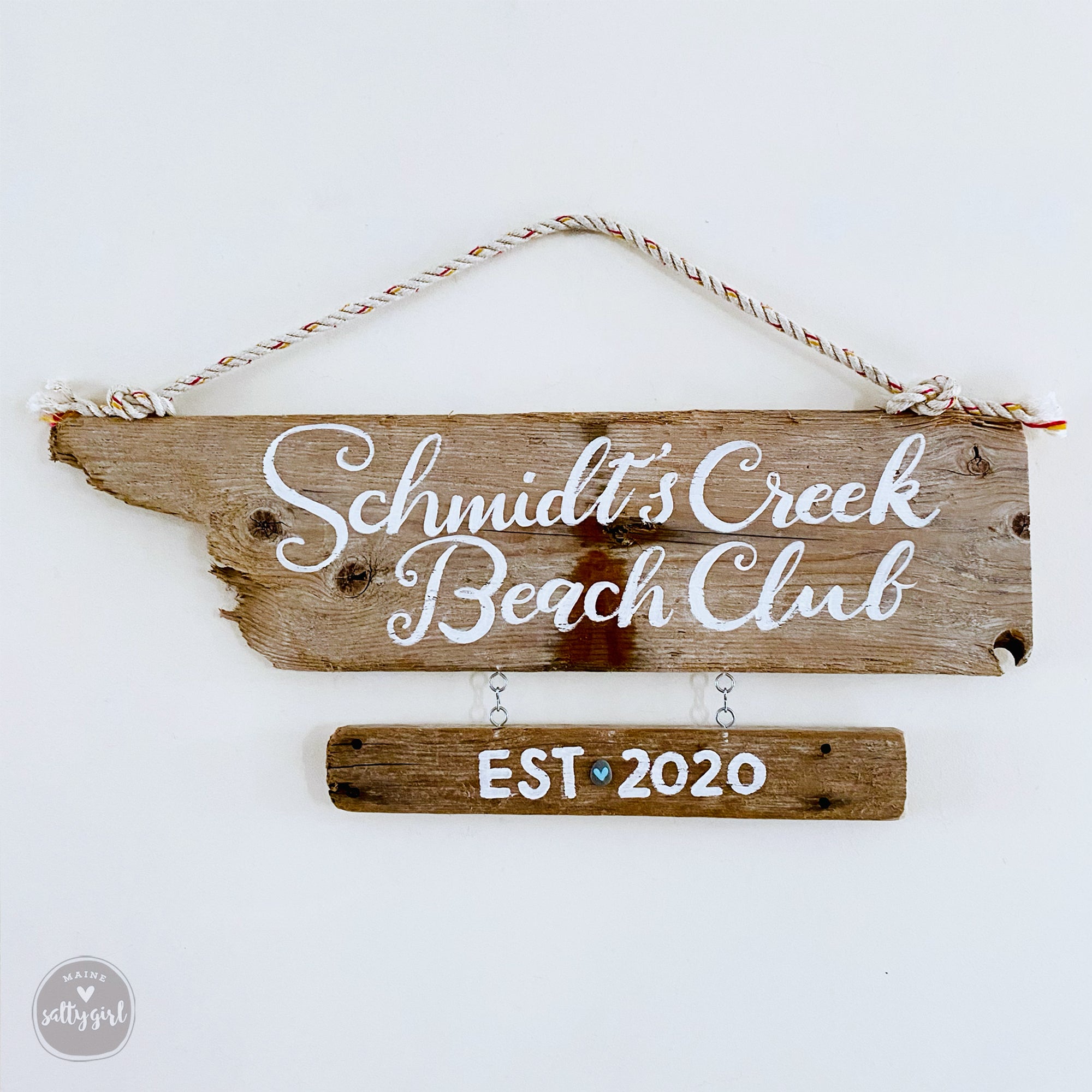 A wooden sign with the text "Schmidt's Creek Beach Club EST 2020" hanging on a wall.
