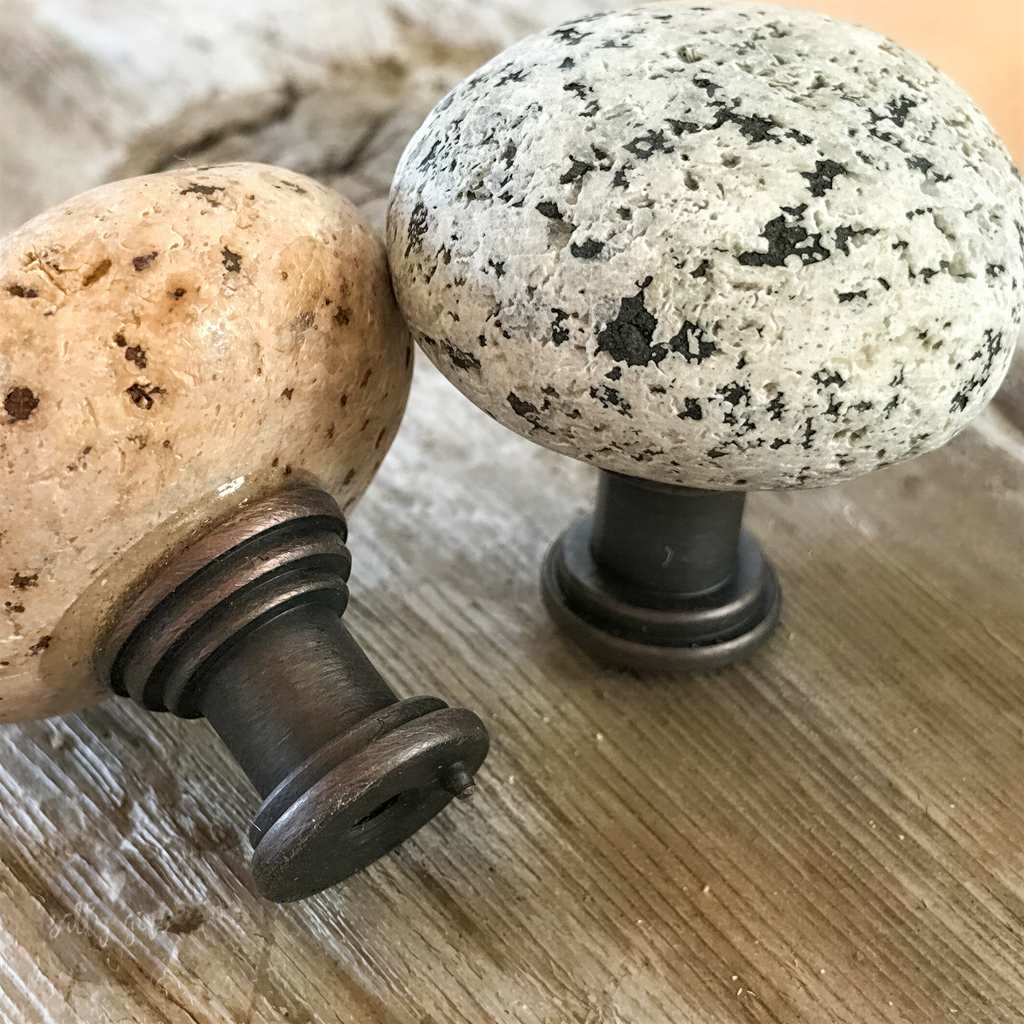two decorative knobs, one with a speckled pattern and the other with a smooth, speckled surface, both resting on a wooden surface.