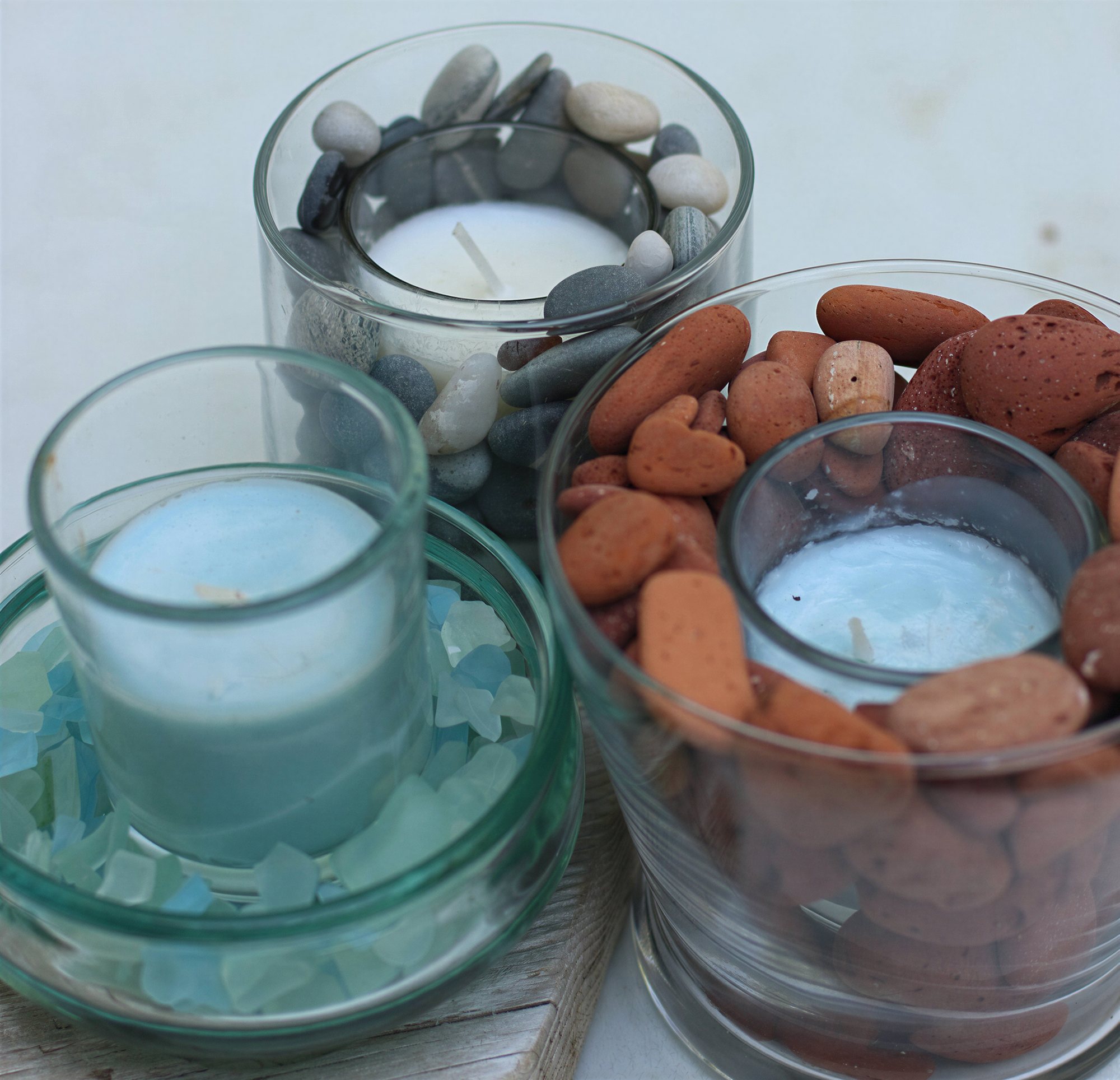 Three glass candle holders with candles in them, each containing different colored stones.
