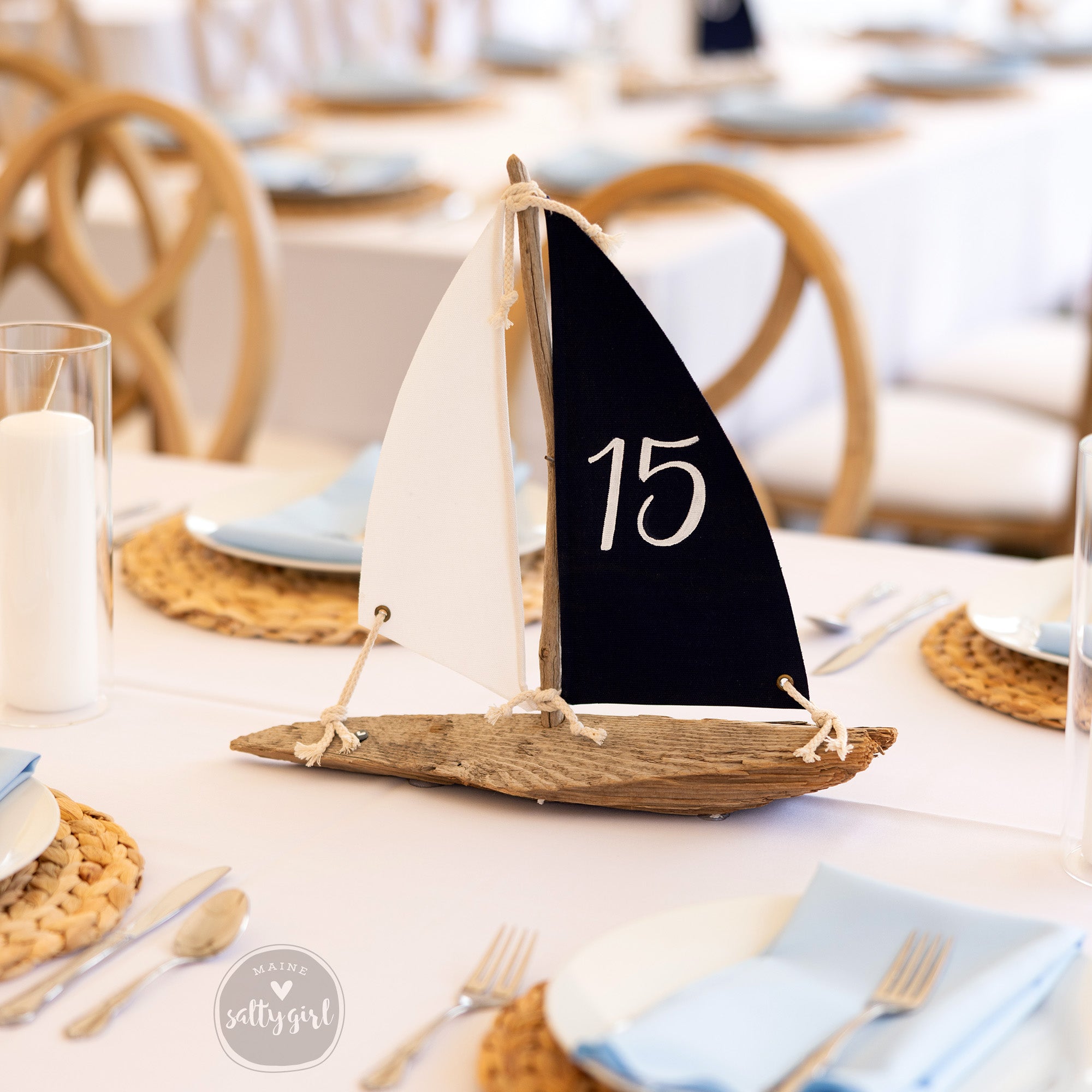 A table setting with a decorative sailboat-shaped centerpiece, featuring a black sail with the number 15 on it, surrounded by place settings and other tableware.