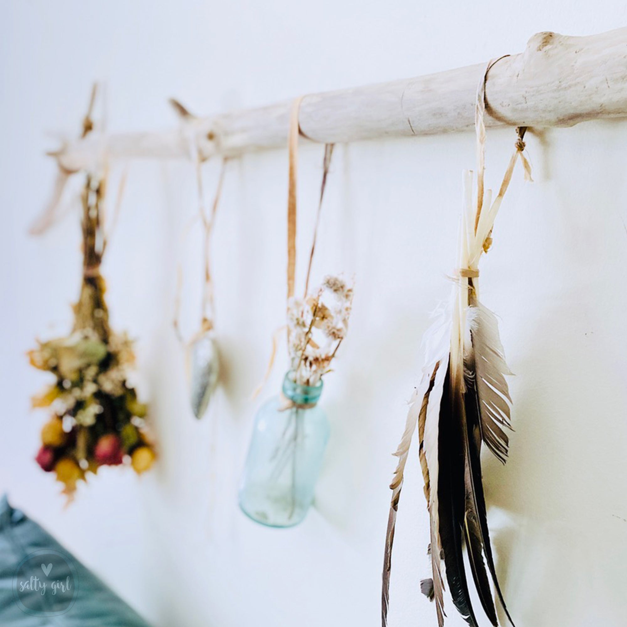 a collection of decorative items hanging on a wooden stick, including feathers, flowers, and a glass jar.
