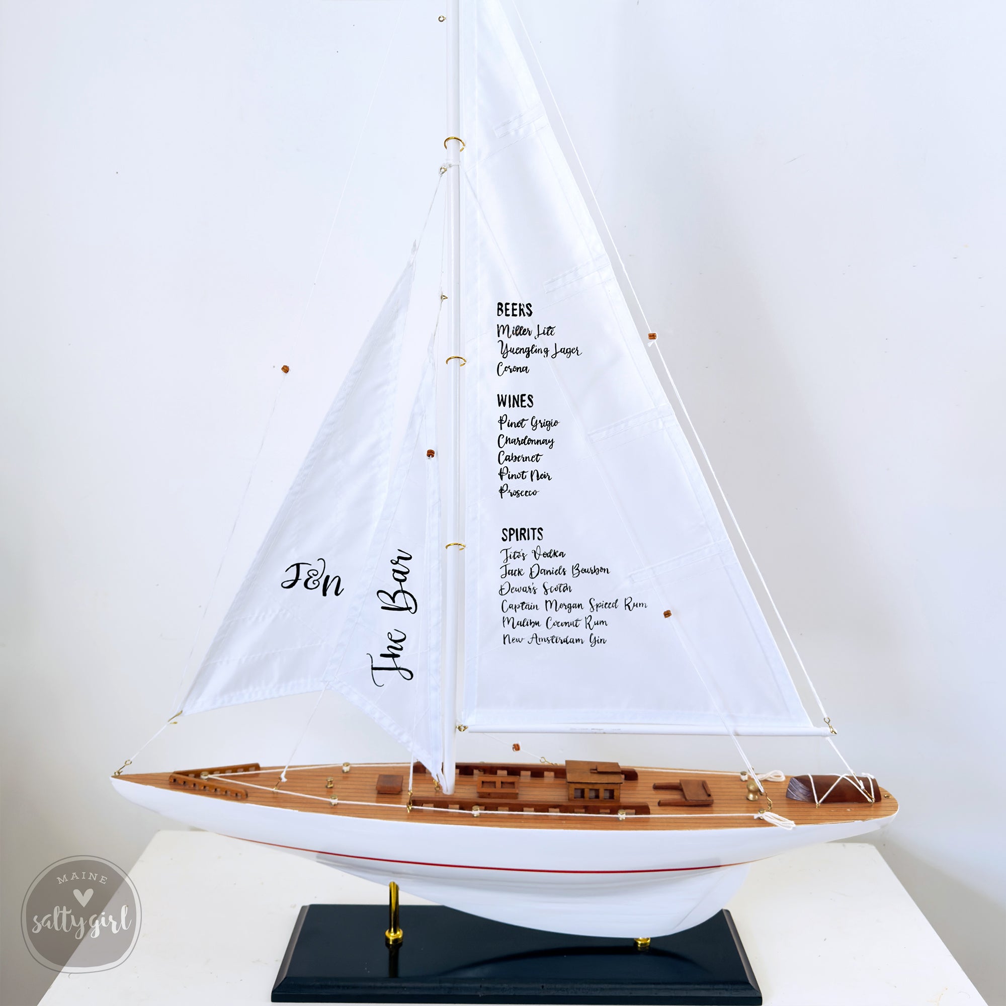 A white sailboat model with a list of drinks displayed on its sails, including beers, wines, spirits, and other beverages.