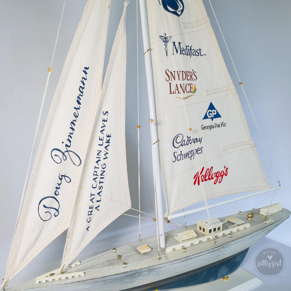 A model sailboat with multiple sails displaying various company logos and names.