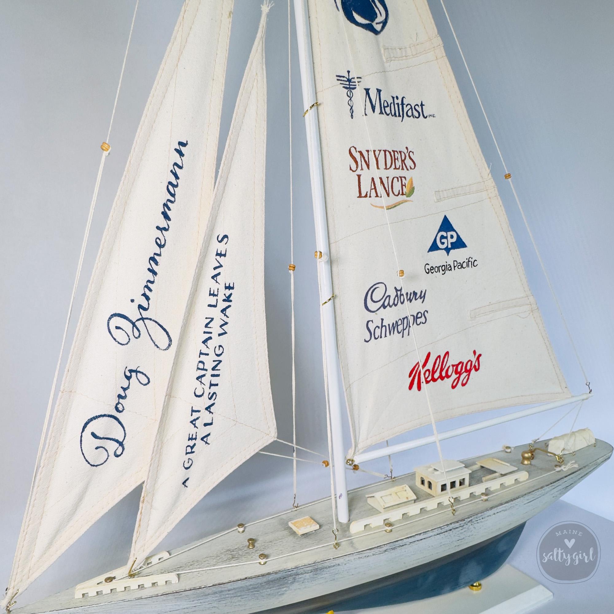A model sailboat with multiple sails displaying various company logos and names.
