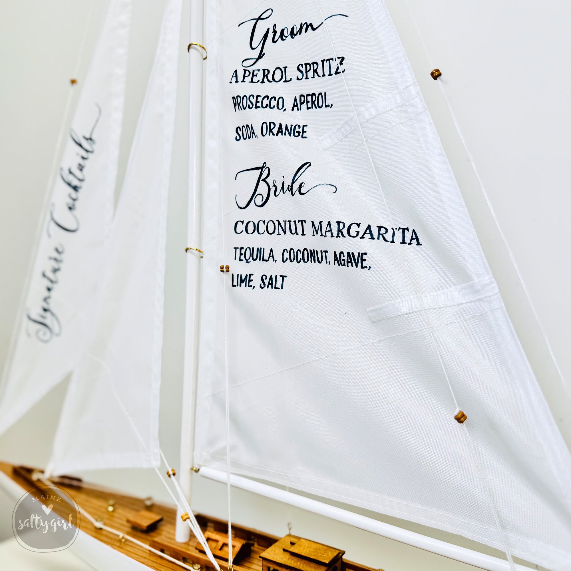 A close-up of a white sailboat with black text on it, displaying the names of drinks such as "Groom" and "Bridle".