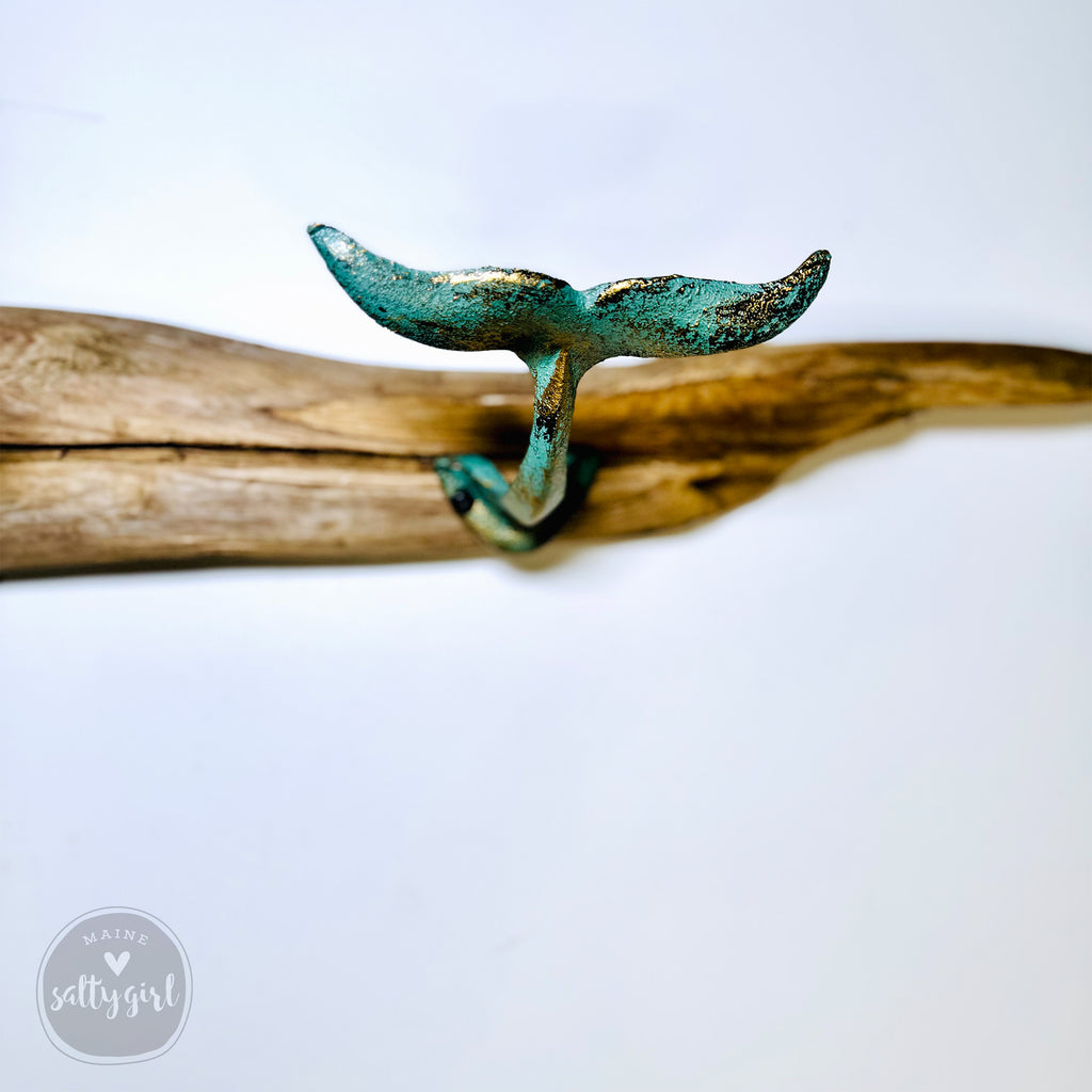A green metal hook with a curved shape is mounted on a wooden board against a white background.