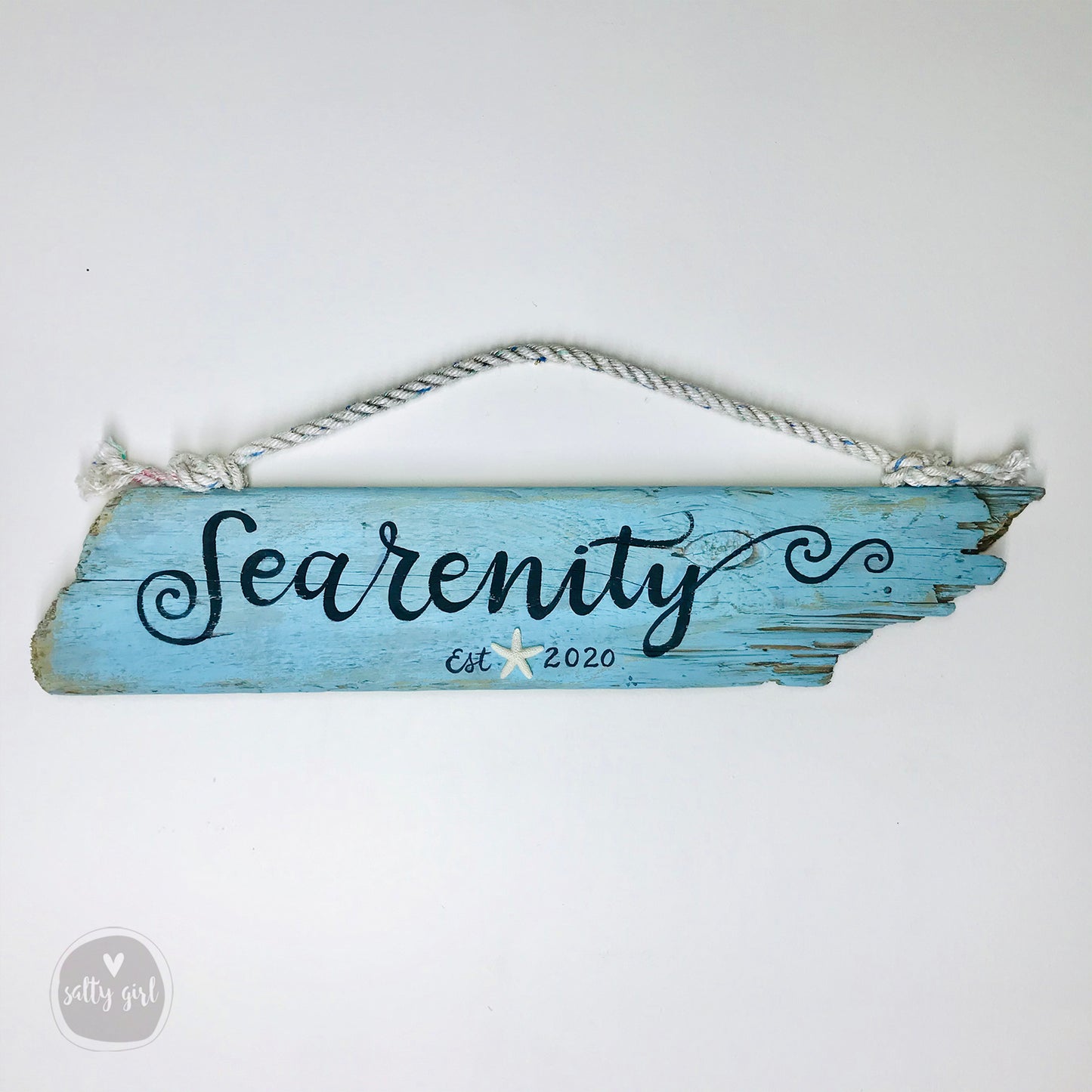 A blue wooden sign with the word "Searenity" written on it, hanging on a rope.
