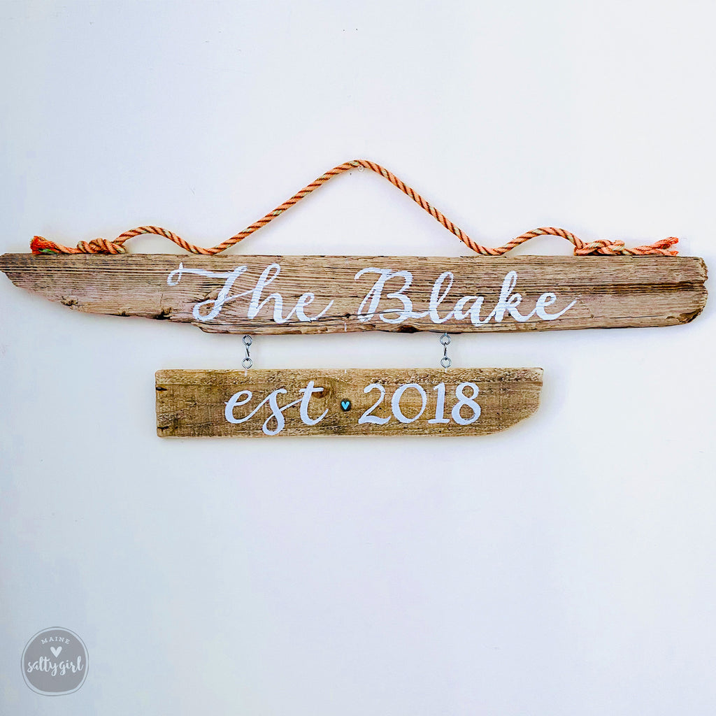 A wooden driftwood sign with the name "The Blake" and the year "2018" written on it, hanging on a wall.