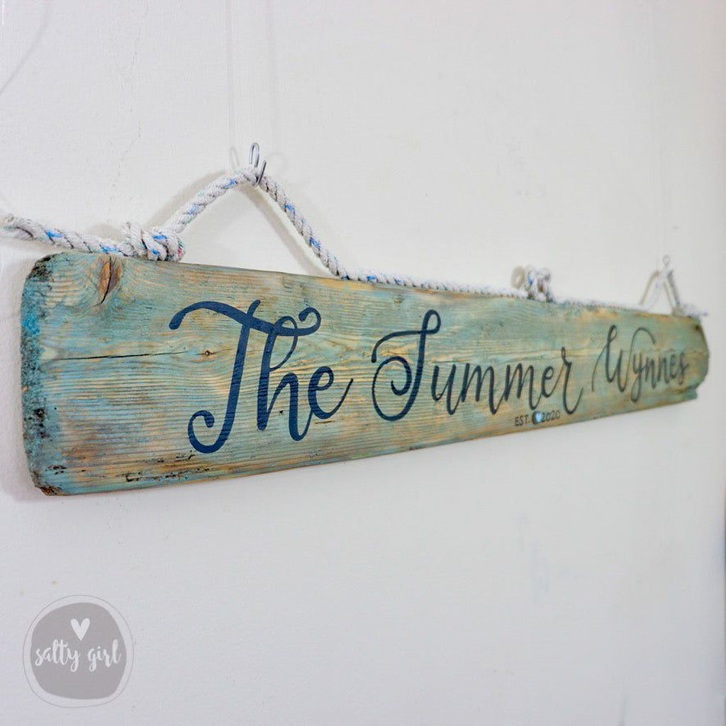 A weathered wooden sign with the text "The Summer Wights" written on it, hanging on a white wall.