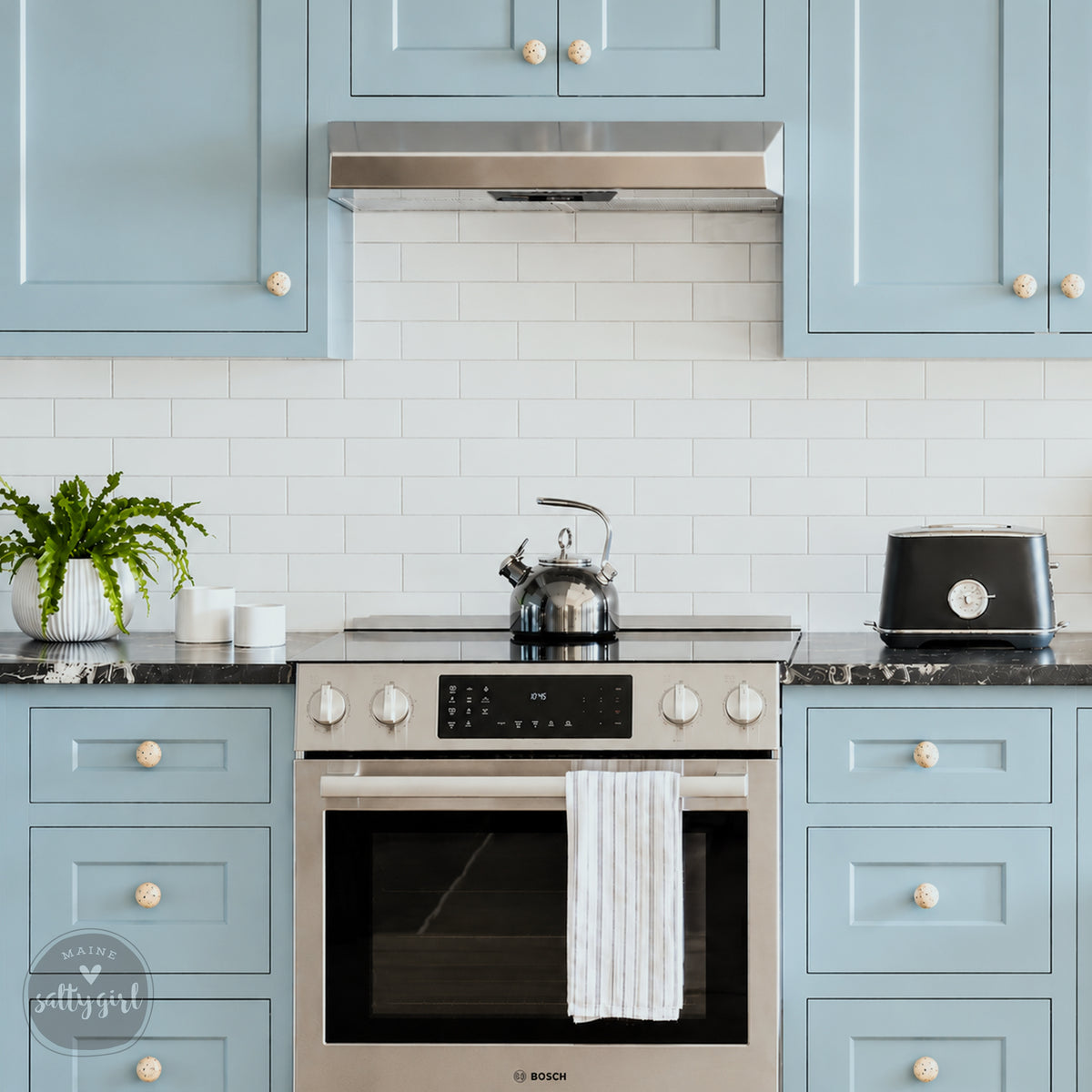 A modern kitchen with light blue cabinets, a stainless steel oven, and a black toaster on the countertop.